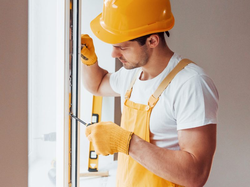 Handyman in yellow uniform installs new window. House renovation conception residential window replacement morrisville pa