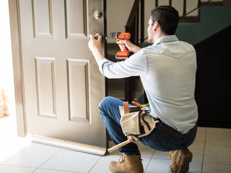 Young man fixing a door lock Rear view of a good looking man working as handyman and fixing a door lock in a house entrance